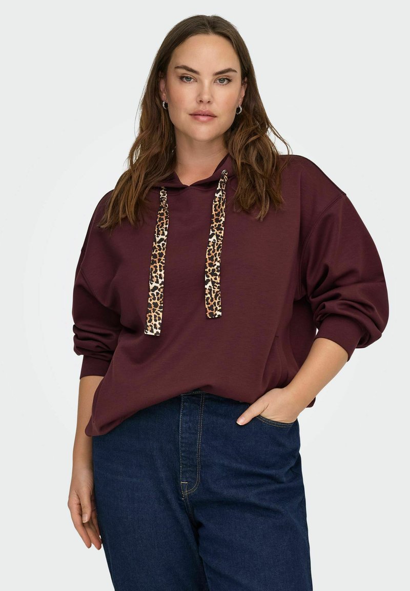 Kastani krāsas kapuce ar leopardu raksta saistēm, pārmērīgi liela izmēra, ar ribinātām aprocēm, apvienota ar tumši ziliem džinsiem. Gluda auduma tekstūra.