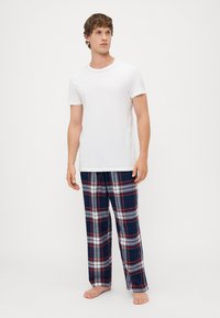 Hvit t-skjorte med korte ermer kombinert med marineblå rutete pysjbukser med røde og hvite striper, laget av myk bomullsstoff.