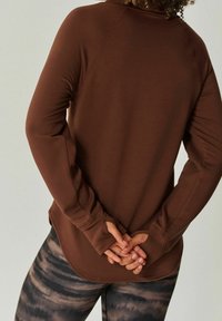 Bruine lange mouw top met raglanmouwen, naadloos ontwerp en een gebogen zoom. Gecombineerd met gemêleerde leggings met een verloop effect.