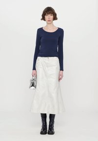Marineblaues Langarmoberteil, silberner metallischer Midirock, schwarze kniehohe Stiefel, hält eine metallische Handtasche. Glatter Stoff, taillierte Passform, schlichtes Design.