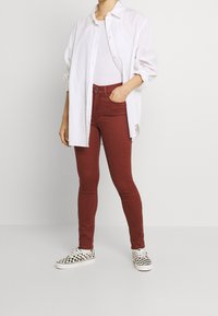 Jeans ajustados rojos combinados con una camisa blanca de botones y zapatos de lona a rayas en blanco y negro. Tela suave, diseño clásico.