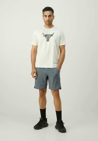 Tricou bărbați gri deschis cu un grafic de taurus negru, asortat cu pantaloni scurți gri închis. Adidași închiși la culoare și șosete negre completează ținuta.
