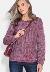 Rot und lila gestrickter Pullover mit einem strukturierten Wellenmuster, langen Ärmeln, rundem Ausschnitt und lockerer Passform, kombiniert mit einer kleinen burgunderfarbenen Tasche.