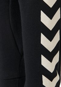 Sweatshirt noir avec un tissu texturé et un motif en chevrons blanc prononcé le long des manches. Encolure arrondie et coupe ajustée.