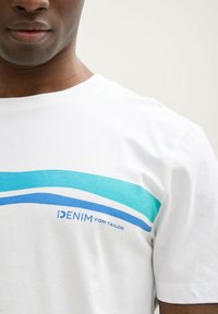 Balta medvilninė marškinėliai, su mėlynomis ir turkio spalvos horizontaliomis juostelėmis per krūtinę, su užrašu "DENIM TOM TAILOR" mėlyna spalva.