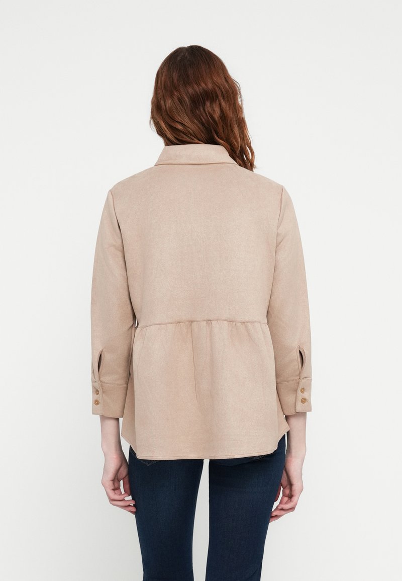 Beige Bluse mit Knöpfen und Peplum-Taille, langen Ärmeln und hochrollbaren Manschetten. Weicher Stoff mit subtiler Glanz, mit Kragen und Rückenfalte.