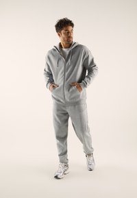 Gray zip-up hoodie with drawstrings, side pockets, and matching sweatpants; worn with silver and gold athletic shoes.