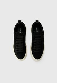 Black suede sneakers with white textured soles and black laces, viewed from above on a plain light background.