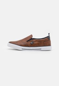 Chaussure en cuir marron à enfiler avec semelle en caoutchouc blanc, accents bleus marine et panneau élastique sur le côté pour un enfilage facile. Présente des détails de couture minimaux.
