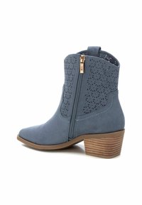 Botas tobilleras de ante azul con diseño perforado, cremallera lateral, punta afilada y tacón de madera apilada. Cuenta con detalles de costura en los bordes.