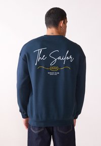 Sudadera azul marino con cuello redondo y mangas largas, que presenta el texto en blanco "El Marinero" y un gráfico de cuerda amarilla en la parte posterior.
