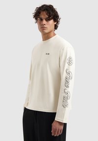 Long-sleeve cream T-shirt, features a small chest logo and black text "Pure Path" on the left sleeve, made from soft cotton material.