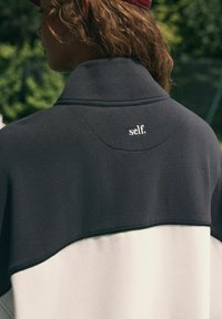 Mustvalge värvikombinatsiooniga sviiter kõrge kaelusega, millel on pehme kangas ja väike "self." logo taga.