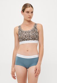 Leopardprint bralette med en hvid elastikbåndmærket "COPENHAGEN STUDIOS," parret med teal boyshorts med et matchende bånd.