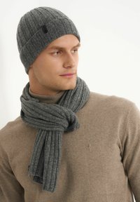 Szara dziana czapka z prążkowanym wzorem i małym czarnym logo. W połączeniu z pasującym szarym prążkowanym szalem, oplecionym wokół beżowego golfu.