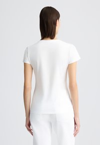 T-shirt blanche ajustée à manches courtes, fabriquée en coton lisse. Col rond classique et design minimaliste sans motifs.