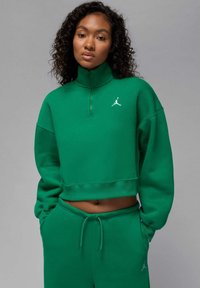 Zielona krótka bluza z wysokim kołnierzem, wykonana z miękkiego materiału, z dyskretnym białym logo na piersi, w zestawie z pasującymi spodniami dresowymi.