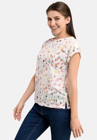 Short-sleeve white top featuring a colorful scattered pebble pattern, made from lightweight fabric with a relaxed fit and side slits.