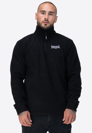 Schwarzer Fleece-Pullover mit hohem Kragen und viertel Reißverschluss. Mit einem kleinen weißen Logo auf der linken Brust. Weiche Textur, lange Ärmel.