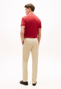 Κόκκινο πόλο πουκάμισο με λευκές ρίγες στο γιακά, συνδυασμένο με μπεζ παντελόνι ίσιας γραμμής, ολοκληρωμένο με μαύρα παπούτσια. Οπίσθια όψη.
