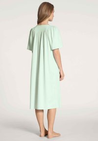 Vestaglia leggera verde menta con maniche corte, dettaglio arricciato sulle spalle e taglio dritto che arriva sotto il ginocchio. Tessuto con una consistenza liscia.
