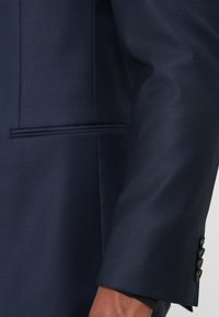 Marineblazer aus strukturiertem Stoff mit klarer Schnittführung, schmaler Passform und drei schwarzen Knöpfen am Ärmelbündchen. Dezente Taschenapplikationen sichtbar.