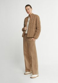 Veste bomber en tricot marron avec un col côtelé, associée à un pantalon large beige clair et des baskets blanches.