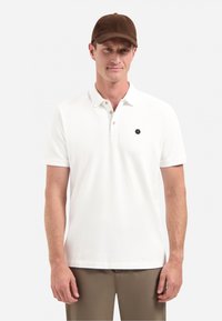 Witte polo met een kraag en drie knopen, voorzien van een hexagonaal logo aan de linkerkant. Bruine pet met een gestructureerd ontwerp.