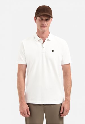 Weißes Poloshirt mit Kragen und drei Knöpfen, versehen mit einem sechseckigen Logo auf der linken Seite. Braune Kappe mit strukturiertem Design.