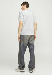 Weißes Baumwoll-T-Shirt mit kurzen Ärmeln, kombiniert mit lockeren blauen Denim-Jeans mit einer ausgewaschenen Textur und zwei Gesäßtaschen.