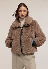 Giacca in ecopelliccia marrone con chiusura a zip, ampio colletto e motivo testurizzato. Dettagli neri sui polsini e sulle tasche frontali.