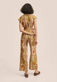 Jumpsuit z szerokimi nogawkami w odcieniu beżowym, z misternymi wzorami kwiatowymi i paisley. Posiada krótkie rękawy oraz pasek w talii, co nadaje mu dopasowaną sylwetkę.