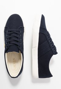 Námořnické modré plátěné tenisky mají bílé gumové podrážky, kulatou špičku, šněrovací design a krémovou podšívku s logem.