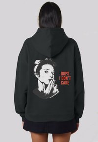 Sudadera con capucha negra que presenta un diseño gráfico en la parte posterior con un retrato en blanco y negro y el texto "OOPS I DON'T CARE" en naranja.