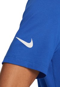 T-shirt in cotone blu con collo rotondo e maniche corte. Logo Nike bianco stampato sulla manica superiore. Texture liscia, design casual.