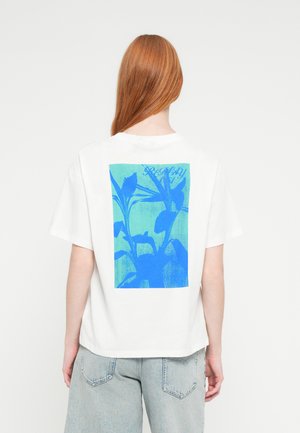 Weißes T-Shirt mit einem blauen Pflanzenmotiv auf der Rückseite. Weicher Baumwollstoff mit lockerem Schnitt und überschnittenen Schultern.