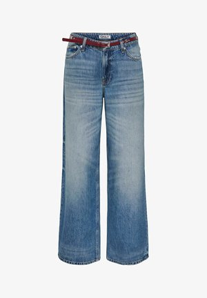 Plačiomis kojomis mėlynos džinsinės kelnės su išblukusio skalbimo detalėmis ir plonu raudonu odiniu diržu, įvertuotu per juosmenį.