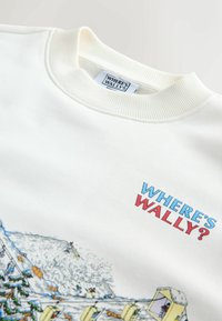White sweatshirt with ribbed crewneck; features “WHERE’S WALLY?” in blue and red lettering; includes a colorful illustration of snowy scenes.