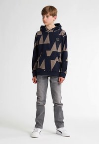 Námořnicky modrá a béžová mikina s geometrickým vzorem a kapucí se šňůrkou, doplněná o šedé džíny a bílé tenisky. Hladká textura látky.