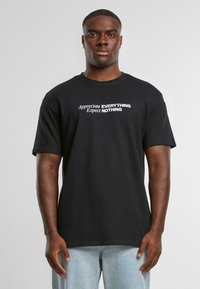 Black cotton t-shirt with short sleeves and crew neck. Features bold text design: "Appreciate EVERYTHING Expect NOTHING" in white.