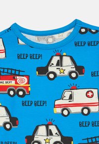 Zila kokvilnas T-kreklu ar atkārtotiem zīmējumiem par kartūnu ārkārtas transportlīdzekļiem, tostarp ugunsdzēsēju mašīnu, policijas automašīnu un ātrās palīdzības auto.