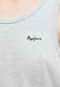 Κοντινή λήψη ενός ανοιχτόγκρι, ριμπ ζανελίνης με μαύρο κεντημένο λογότυπο "Pepe Jeans" στην περιοχή του στήθους.