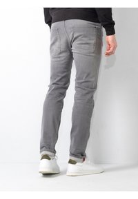 Jeans gris ajustados con bolsillos traseros, costuras en contraste y un ligero desvanecimiento. Combinados con zapatillas blancas con acentos verdes.