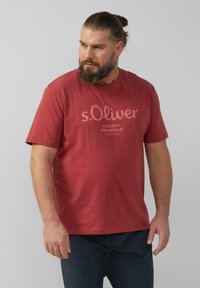 Camiseta de algodón roja con mangas cortas y cuello redondo. Presenta el logo de s.Oliver y texto en un tono más claro. Diseño liso, sin patrones.