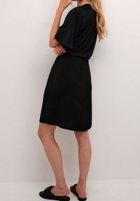 Svart, knälång klänning med avslappnad passform, korta ärmar och elastisk midja. Slät textur utan synliga mönster eller detaljer.