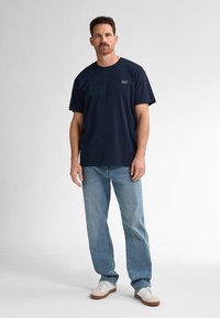 Námořnická modrá bavlněná tričko s krátkým rukávem, se malým obdélníkovým štítkem. V kombinaci s světlými modrými džíny a bílými teniskami.