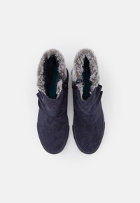 Par de botas de invierno de ante azul oscuro con forro de pelaje sintético gris, vistas desde arriba sobre un fondo blanco.