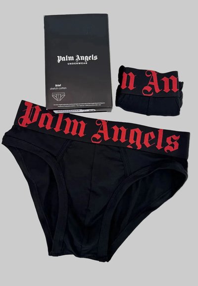 Μαύρα εσώρουχα Palm Angels με κόκκινη λωρίδα μέσης με λογότυπο, διπλωμένα εσώρουχα σε ταιριαστό χρώμα και μαύρο κουτί συσκευασίας σε γκρι φόντο.