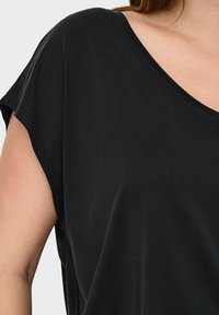 Haut noir à manches courtes avec un large col en V, fabriqué dans un tissu doux. Il présente une coupe décontractée, une texture lisse et sans motifs ou accents visibles.