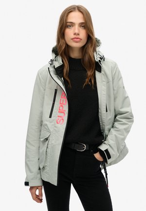 Lys grå vandtæt jakke med sorte accenter, lynlås foran, snor-hætte og stort pink "SUPER" print på siden. Tekstureret sort sweater underneath.